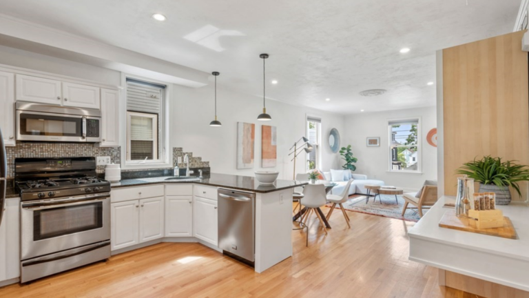 Living room and kitchen connected via open floor plan. The space has pendant lighting, hardwood floors, and single-hung windows.