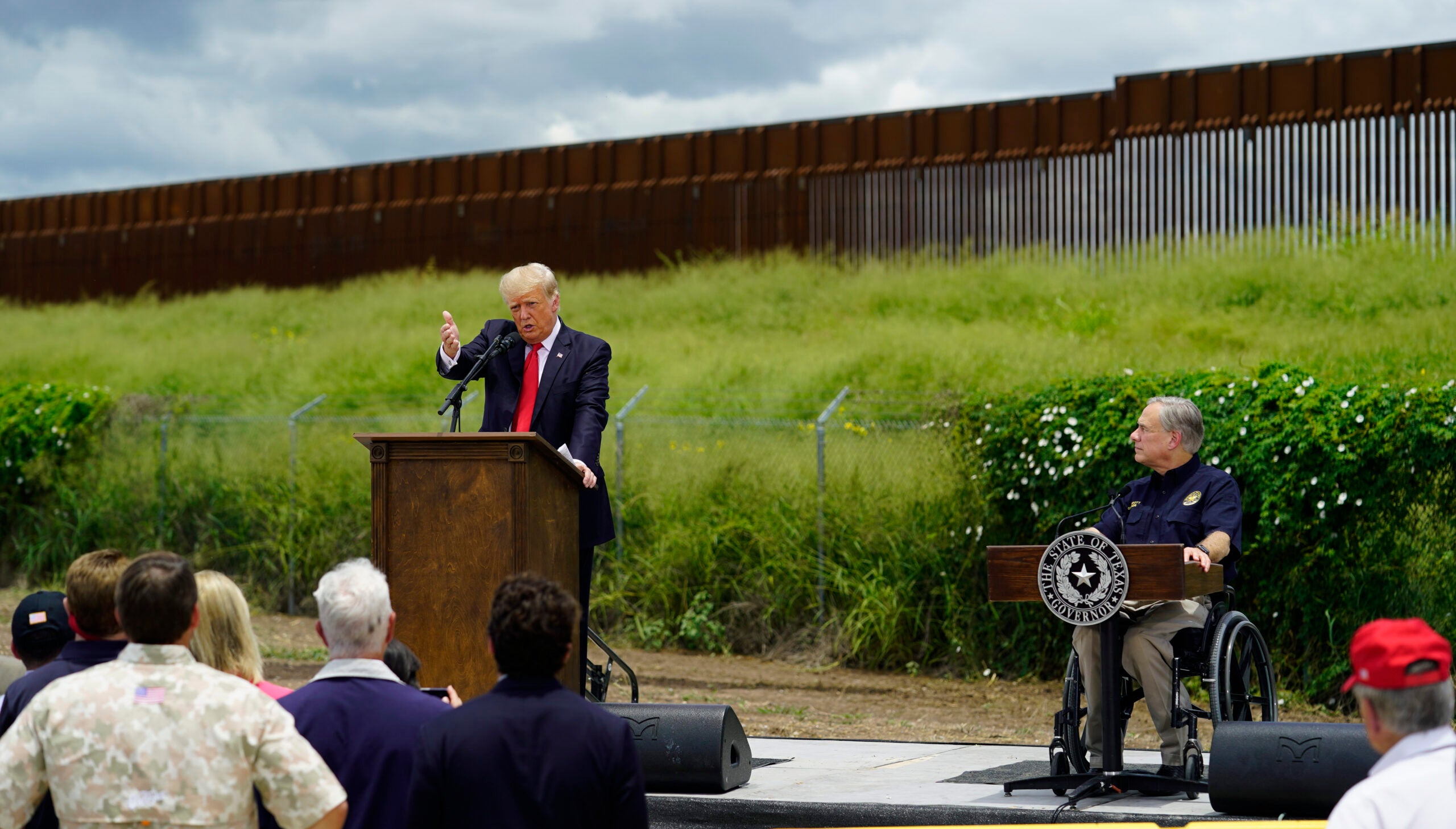 Texas Gov. Greg Abbott, right, listens to Former President Donald Trump, left, during a visit to an unfinished section of border wall, in Pharr, Texas.