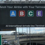 A road sign reads: "Welcome to Logan International Airport. Match your airline with your terminal letter." The letters A, B, C, and E are listed; D is missing.