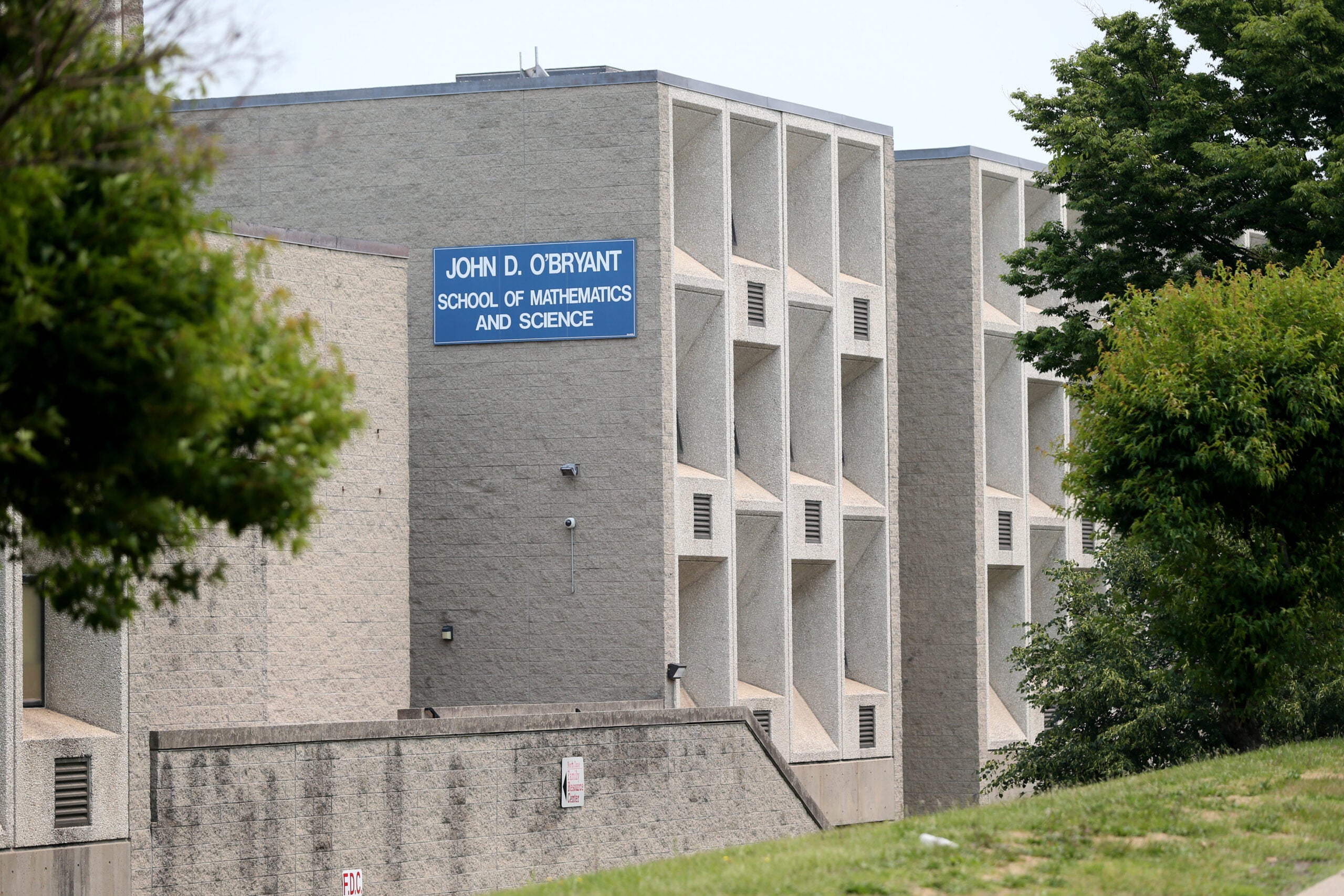 A light gray concrete building sits in the distance, a bright blue sign with white lettering reading, 