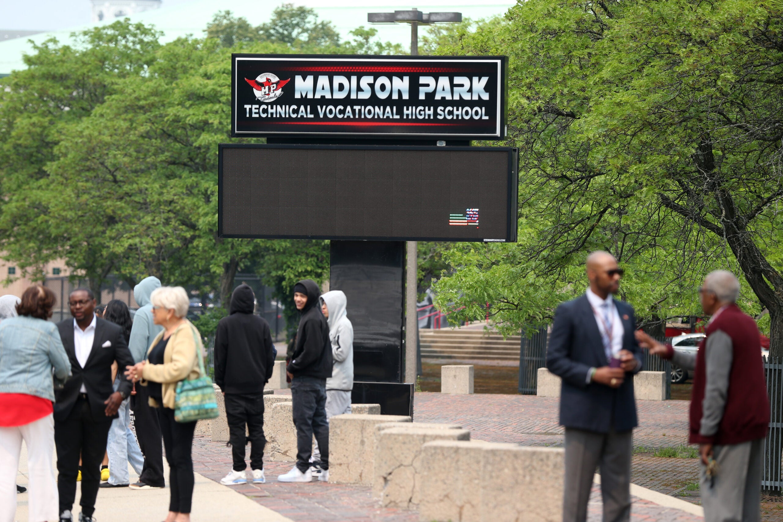 A few people are seen milling around an empty courtyard with a tall sign that reads "Madison Park Technical Vocational High School."