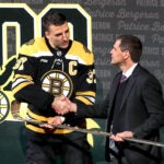 Patrice Bergeron is presented a gold hockey stick by Don Sweeney as he was honored for his 1000th career point.