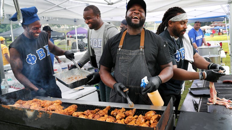 Chef Brian Alleyne, center, has a chuckle as he cooks chicken legs on his charcoal grill