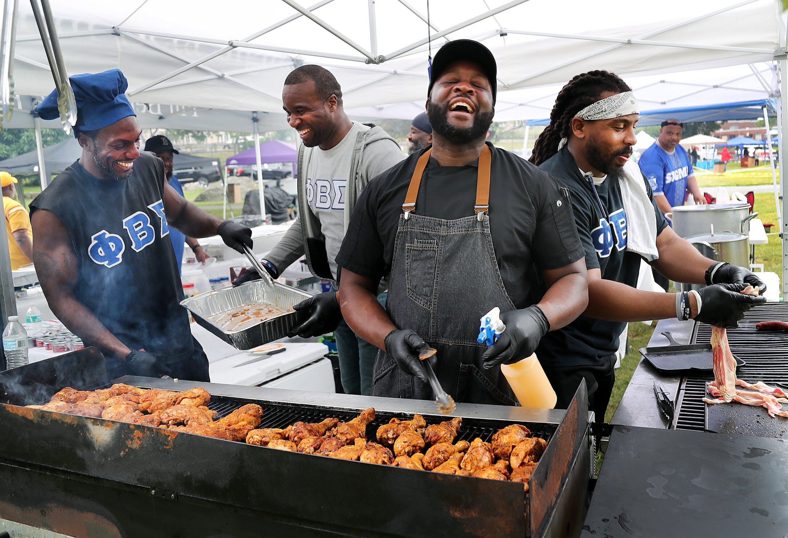 Chef Brian Alleyne, center, has a chuckle as he cooks chicken legs on his charcoal grill