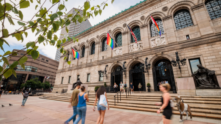 People walk up the steps to the Boston Public Library in Copley Square. Pride flags are seen on the building.