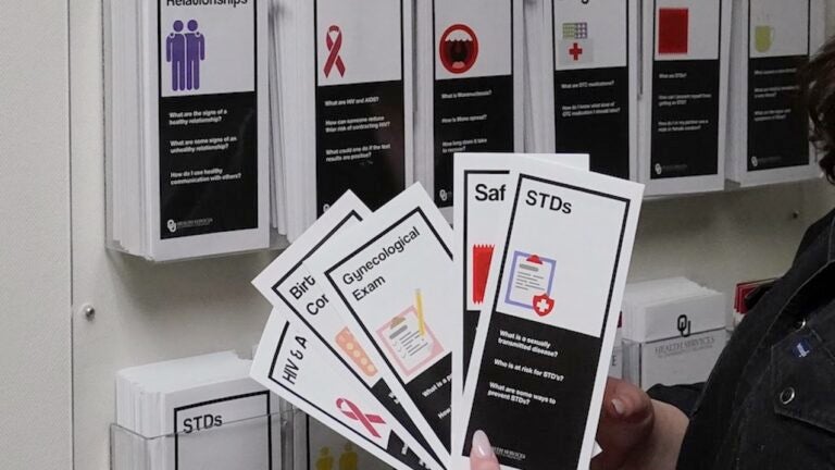 A person is standing out of frame, holding a handful of pamphlets about sexual education, with topics ranging from birth control to STDs.