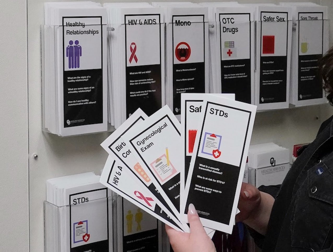 A person is standing out of frame, holding a handful of pamphlets about sexual education, with topics ranging from birth control to STDs.