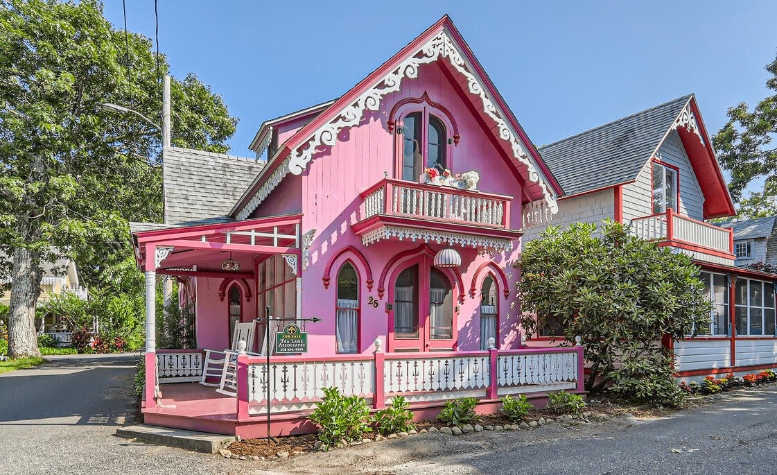 A pink home with white gingerbread trim and a wraparound deck.
