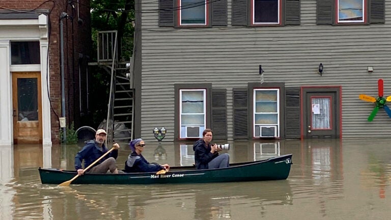 Three people in a canoe paddle through floodwaters along Elm Street in Montpelier, Vt.
