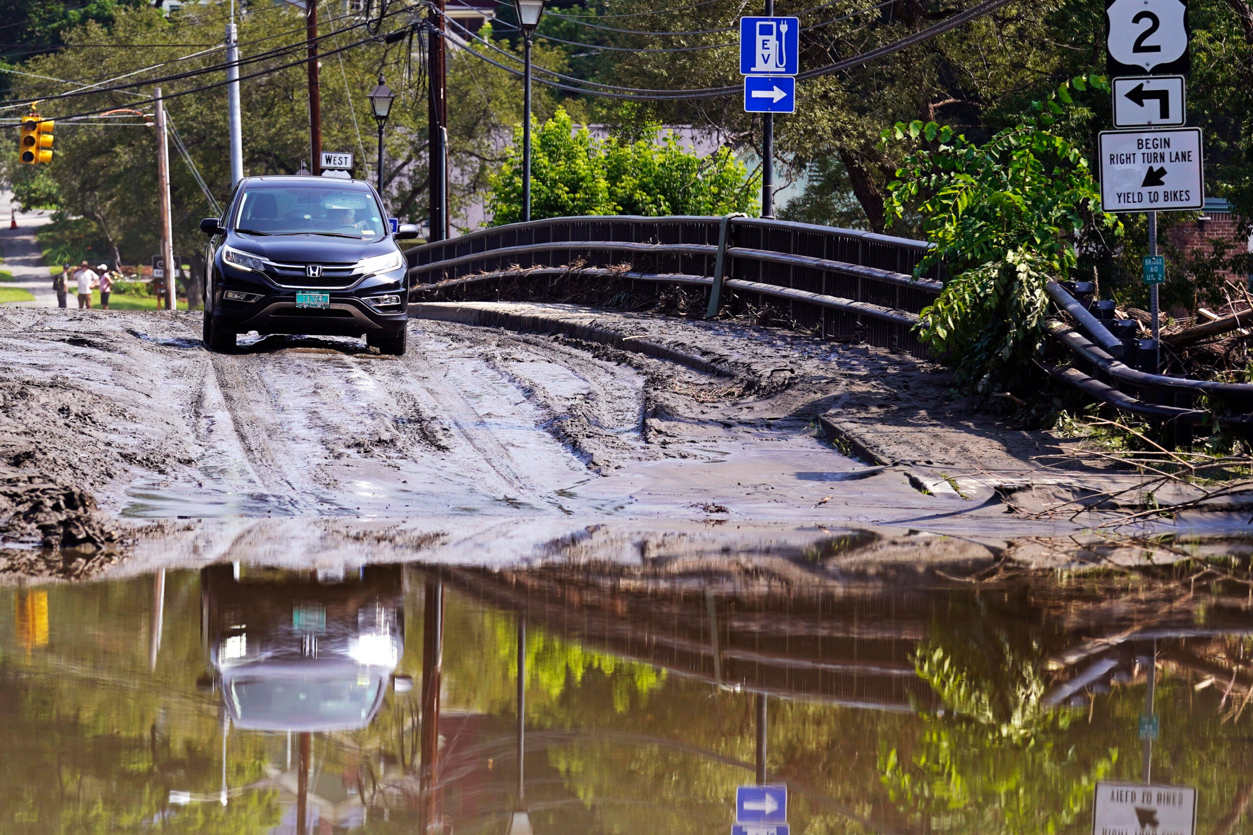 A driver stops on a mud-covered bridge while deciding whether to drive through flood waters of the Winooski River.