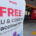 A woman arrives at a CVS pharmacy past a sign about free flu and Covid-19 vaccine.