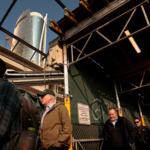 Pedestrians walk in single file beneath scaffolding.