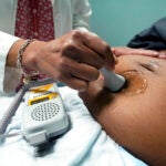 A doctor uses a hand-held Doppler probe on a pregnant woman.