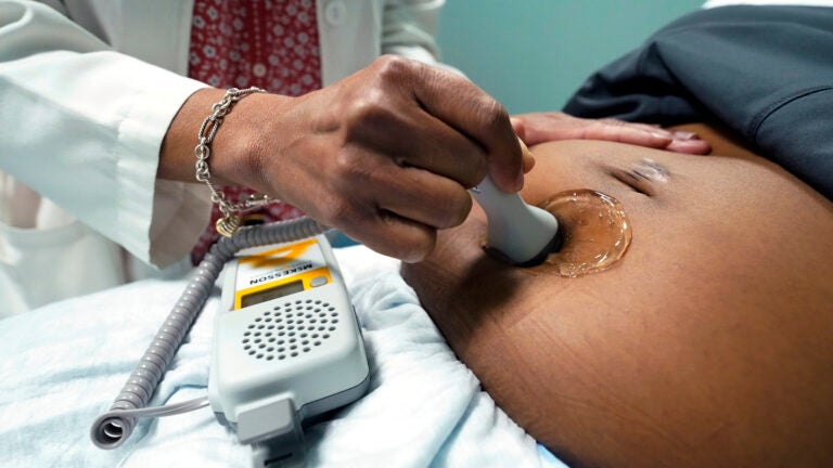 A doctor uses a hand-held Doppler probe on a pregnant woman.