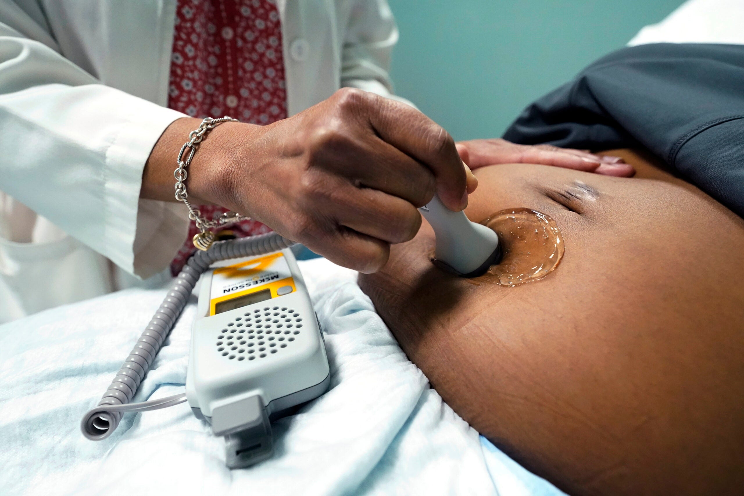 A doctor uses a hand-held Doppler probe on a pregnant woman.