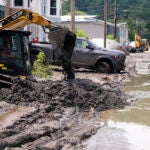 Equipment clears mud from a neighborhood as flood waters block a street.