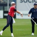 New England Patriots quarterback Mac Jones, left, follows through on a pass in front of offensive coordinator Bill O'Brien, right, during NFL football practice, Tuesday, June 6, 2023, in Foxborough, Mass.