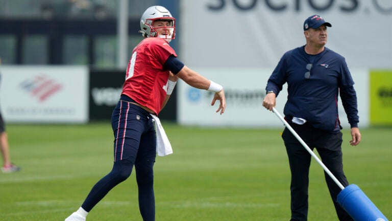 New England Patriots quarterback Mac Jones, left, follows through on a pass in front of offensive coordinator Bill O'Brien, right, during NFL football practice, Tuesday, June 6, 2023, in Foxborough, Mass.