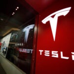 FILE - A sign bearing the Tesla company logo is displayed outside a Tesla store in Cherry Creek Mall in Denver, Feb. 9, 2019.