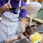 Ice cream scooper, Sam Jacobson, 22, who is entering his 7th season at the store, creates the shop's signature banana split sundae at Kimball Farms in Westford, Mass., on Friday, Jul. 27, 2018.