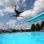 A lifeguard jumps off a diving board into a pool in Newton, MA.