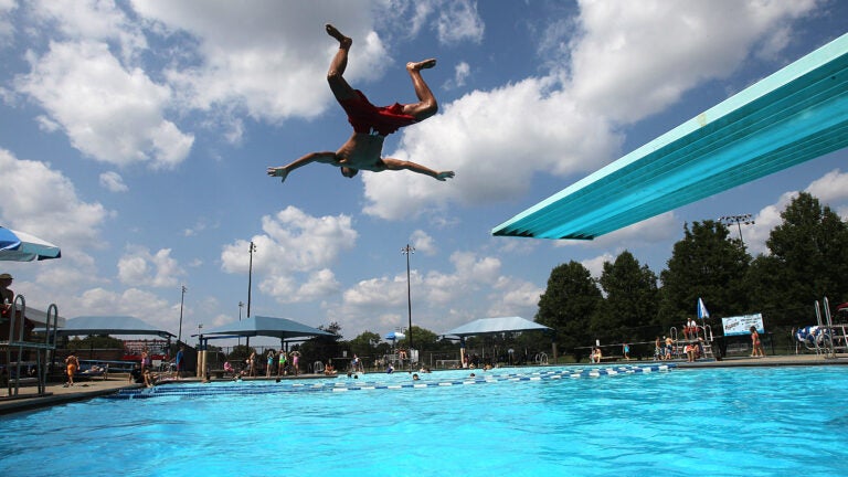 A lifeguard jumps off a diving board into a pool in Newton, MA.