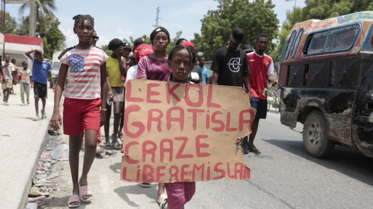 A girl carries a sign that reads in Creole "Free school is broken. Release the nurse," during a march.