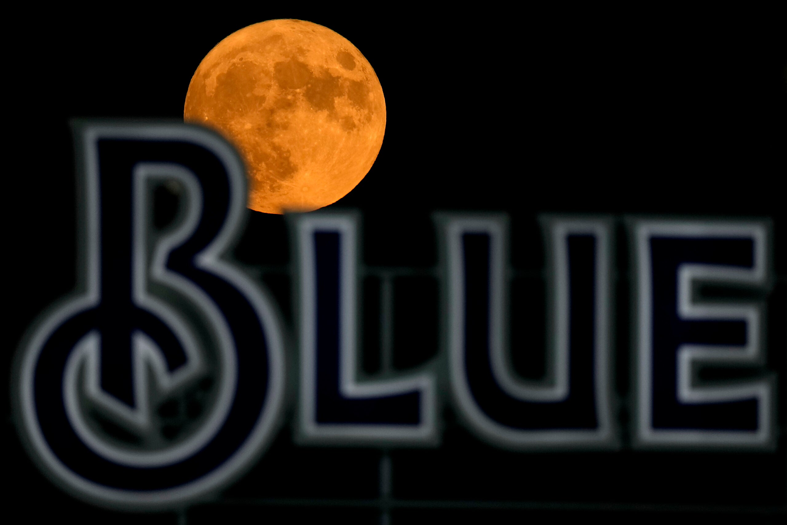 The full moon rises beyond a sign in the outfield during a baseball game.