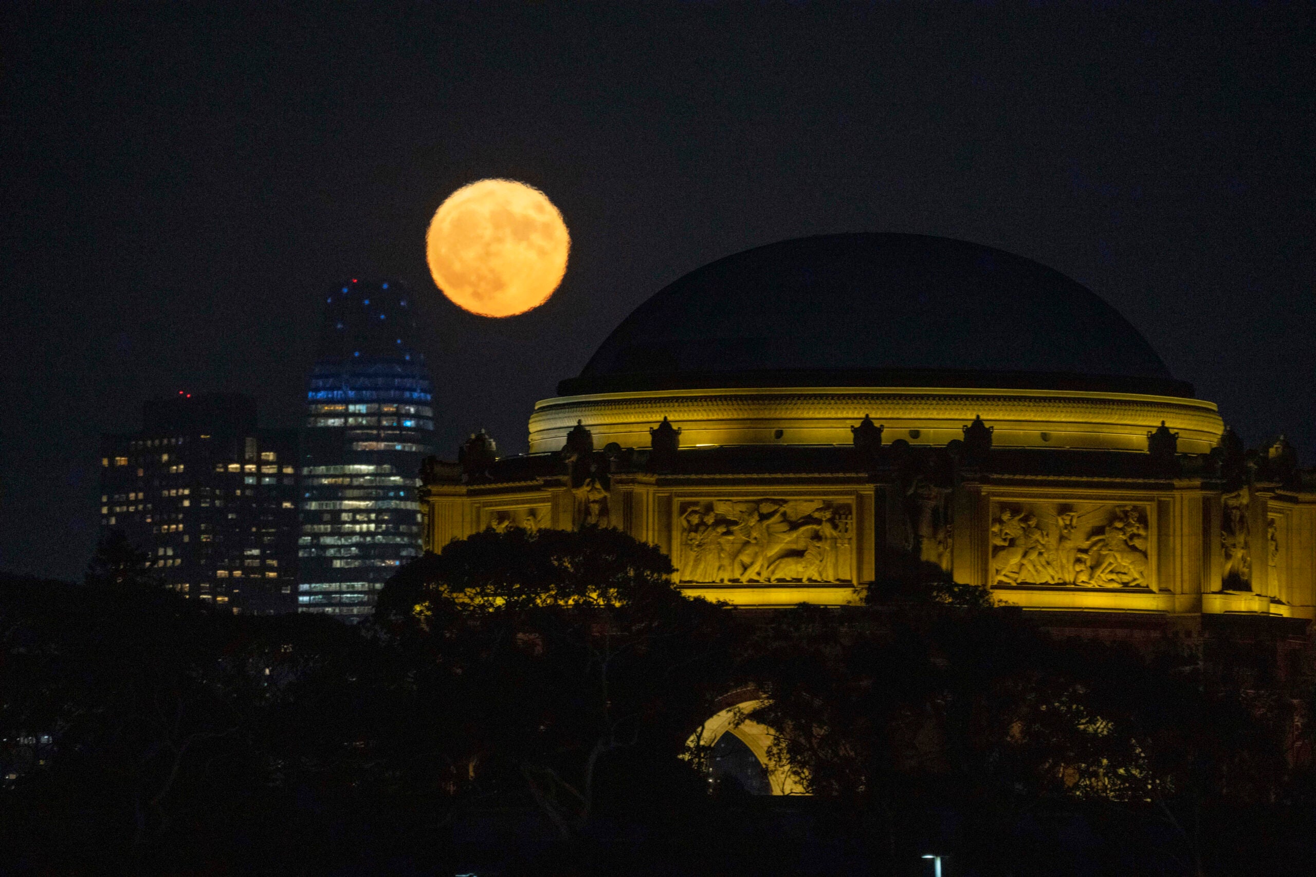 A blue supermoon rises between the Salesforce Tower and the Palace of Fine Arts in San Francisco.