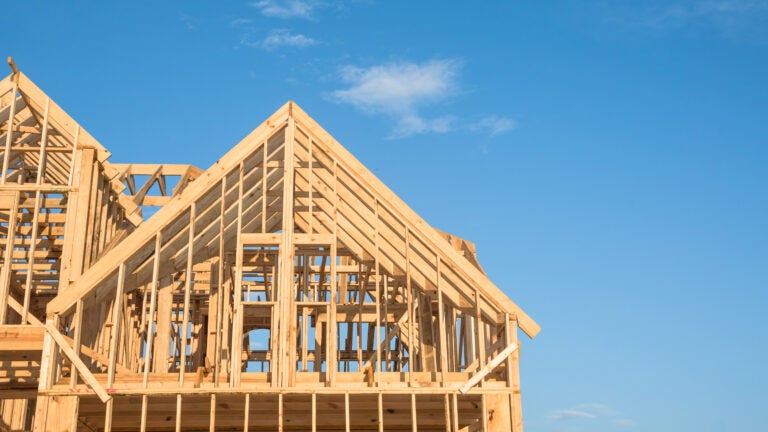 Close-up of gables roof on stick built home under construction and blue sky in Humble, Texas, USA. New build roof with wooden truss, post and beam framework. Timber frame house, real estate. Panorama