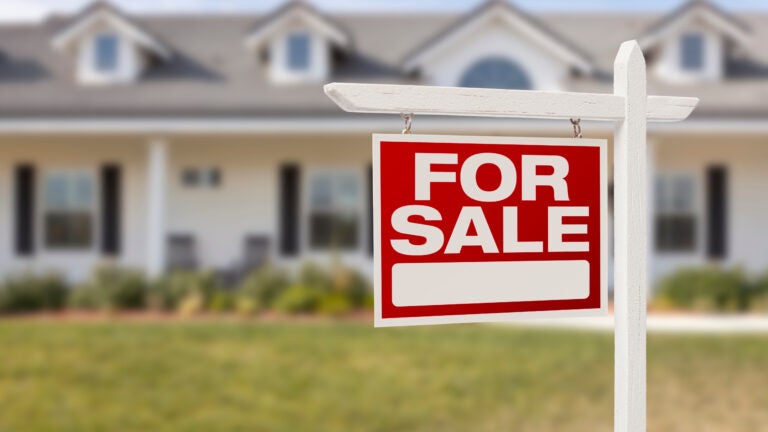For Sale sign in front of blurred background of a house.