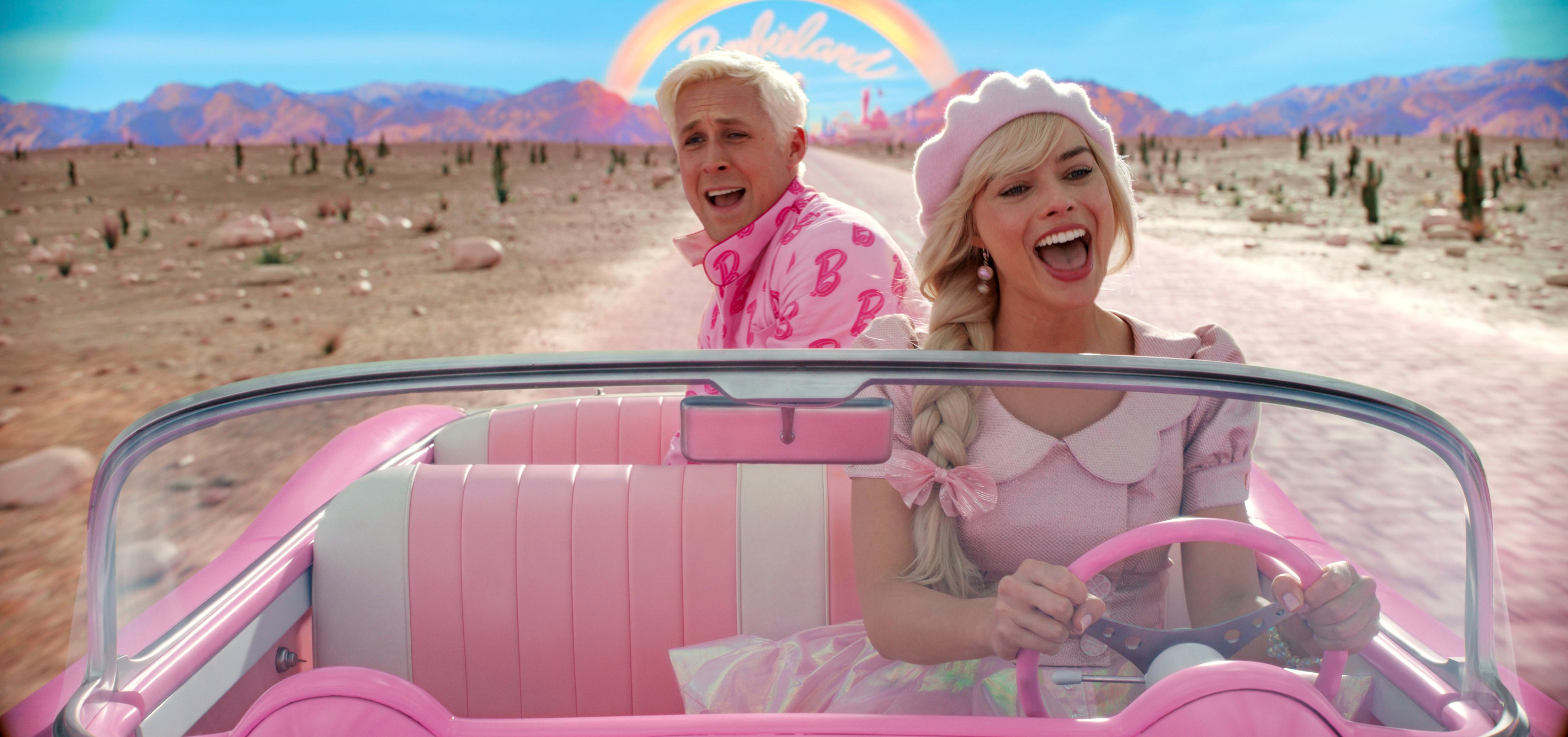 Ryan Gosling and Margot Robbie as Ken and Barbie in a scene from "Barbie." They're driving through a desert in a pink convertible, singing a song.