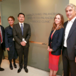 A group of people poses in front of a sign for the newly-renamed Eliza Dushku Palandjian and Peter Palandjian Bridge Clinic.