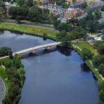 An aerial view of a bending river with a bridge connecting the two banks.