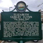 A dark green historical marker with white lettering dedicated to Elizabeth Gurley Flynn in Concord, New Hampshire.