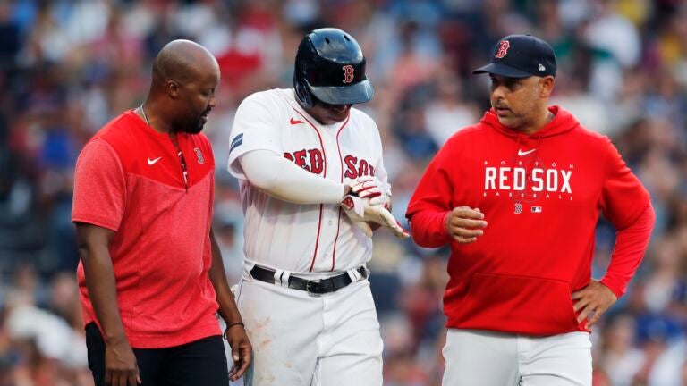 A Boston Red Sox trainer and manager Alex Cora check on Rafael Devers after he was hit by a pitch during the eighth inning of a baseball game, Saturday, Aug. 26, 2023, in Boston.