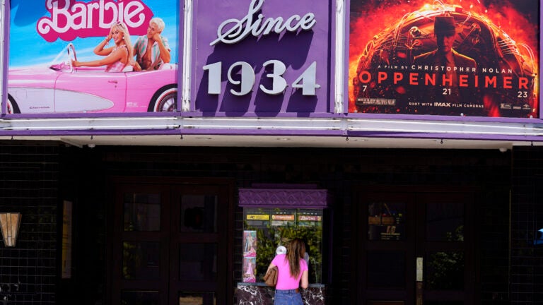 A patron buys a movie ticket underneath a marquee featuring the films "Barbie" and "Oppenheimer."