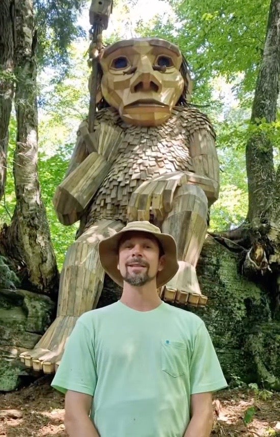 Artist Thomas Dambo stands in front of a wooden troll he made in the Vermont woods.