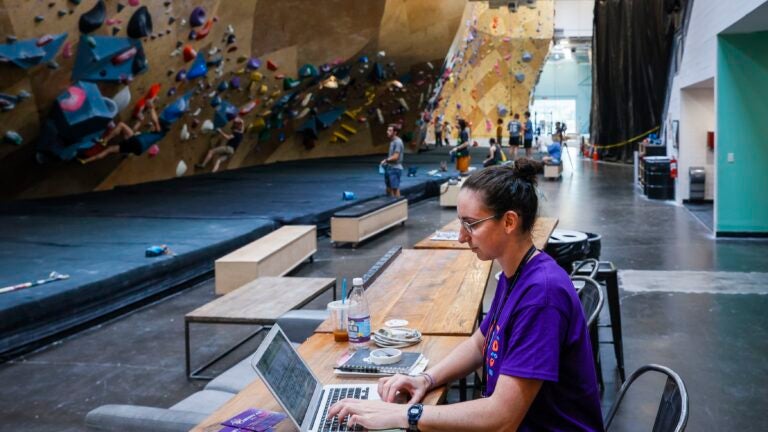 Laura Macdonald, youth programs manager at the Boston Bouldering Project, works from a co-working table nearby the bouldering wall on Aug. 4, 2023.