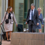 A woman and a man dressed in business attire exit a building