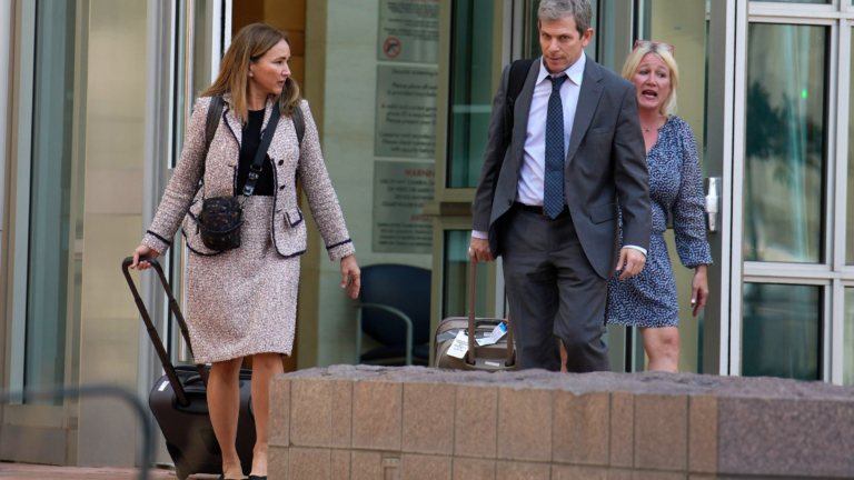 A woman and a man dressed in business attire exit a building