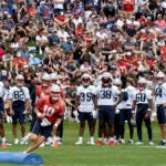 Fans watch the New England Patriots offensive line, including quarterback Mac Jones (10), run drills during an NFL football practice, Sunday, July 30, 2023, in Foxborough, Mass.