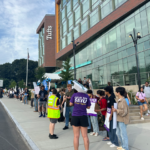 A group of students and young people holding signs in front of a Tufts academic building
