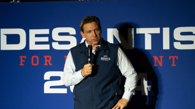 Ron DeSantis speaks into a microphone in front of a 