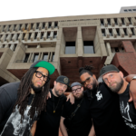 The five members of STL GLD pose for a photo outside Boston's brutalist City Hall building.