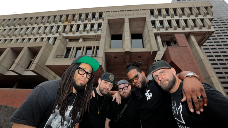 The five members of STL GLD pose for a photo outside Boston's brutalist City Hall building.