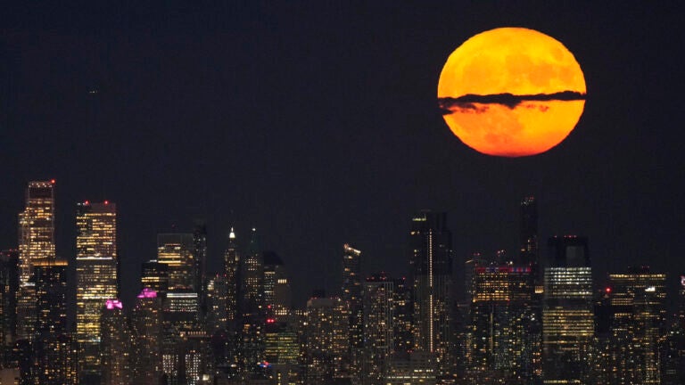 A supermoon rises through clouds over the skyline of lower Manhattan.