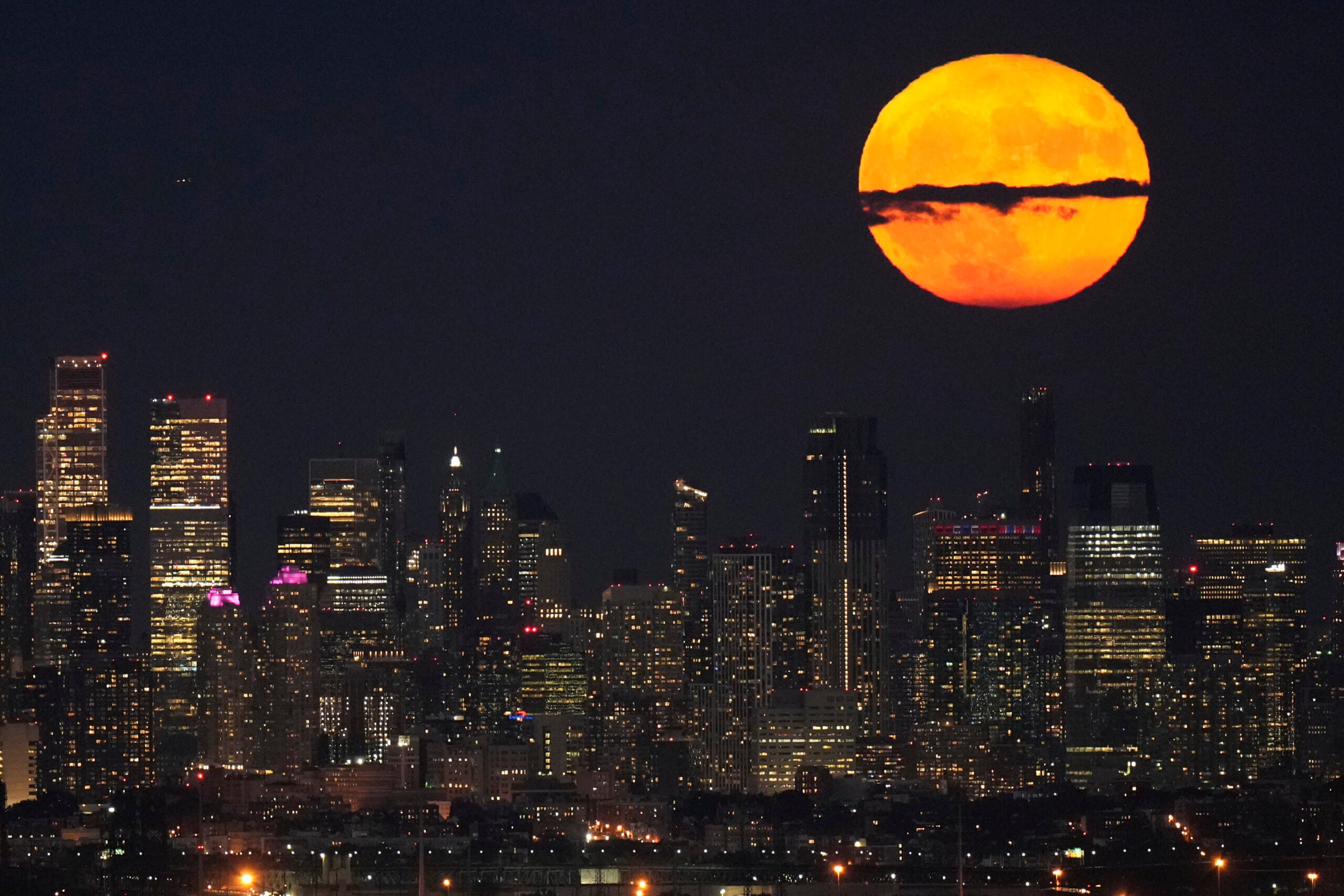 A supermoon rises through clouds over the skyline of lower Manhattan.