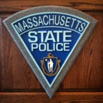 An image of the Massachusetts State Police logo against a wooden wall.