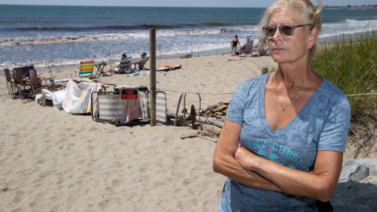 Laurie Bates poses for a photo on the beach in front of her home on Ocean Avenue on the eastern end of East Matunuck Beach in Jerusalem, Narragansett, R.I., on August 9. Bates has expressed frustration over the makeshift barrier her neighbor has created to block off their portion of the beach, at left, and considers it an eyesore and unnecessary.